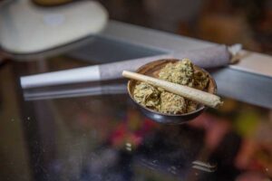 Schale mit Cannabisblüten und Joint als Inhalt, im Hintergrund überdurchschnittlich großer Joint